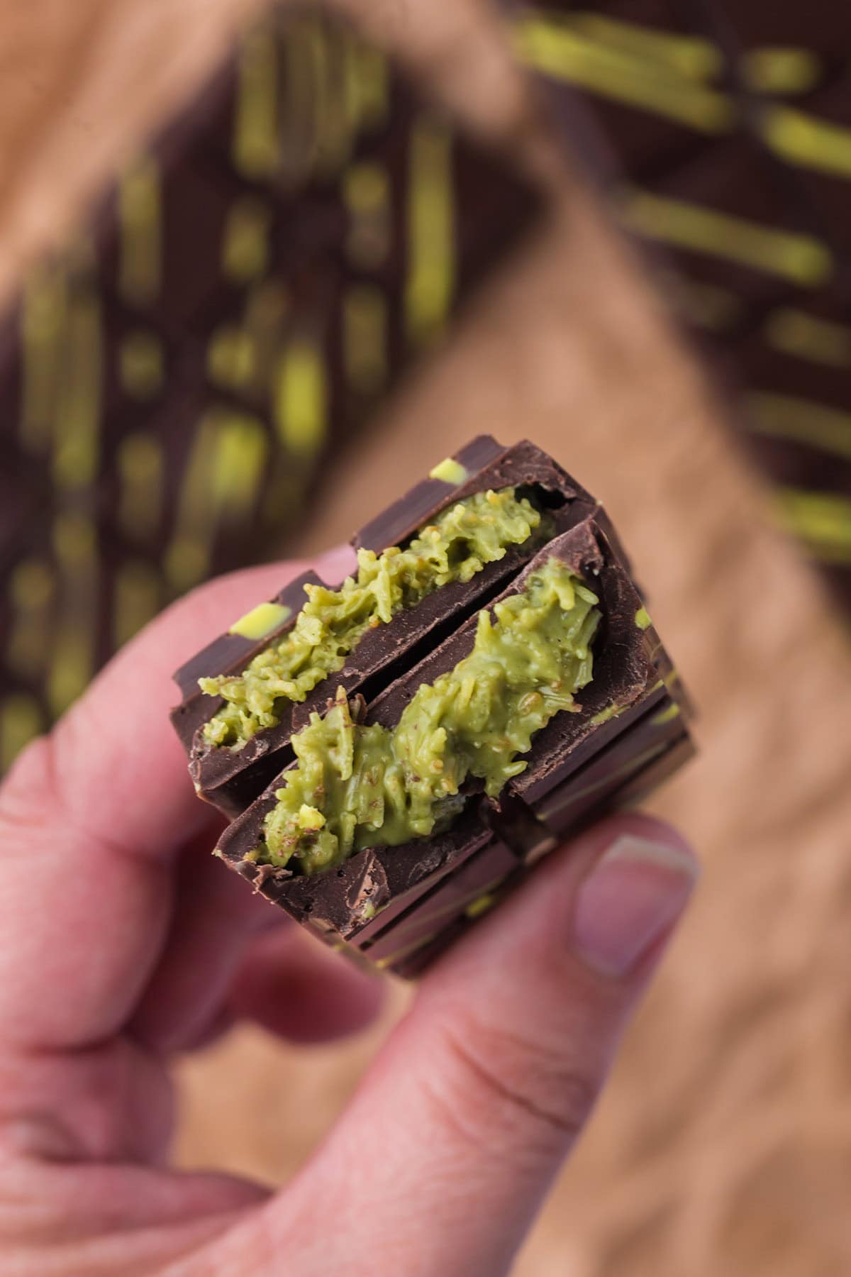 A hand holding a piece of dubai chocolate bar filled with green kataifi filling.