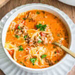 Lasagna soup topped with fresh parsley and shredded cheese in a white bowl.