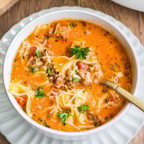 Lasagna soup topped with fresh parsley and shredded cheese in a white bowl.