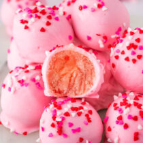 Pink Valentine Oreo truffles with heart sprinkles, one bitten to show the center.