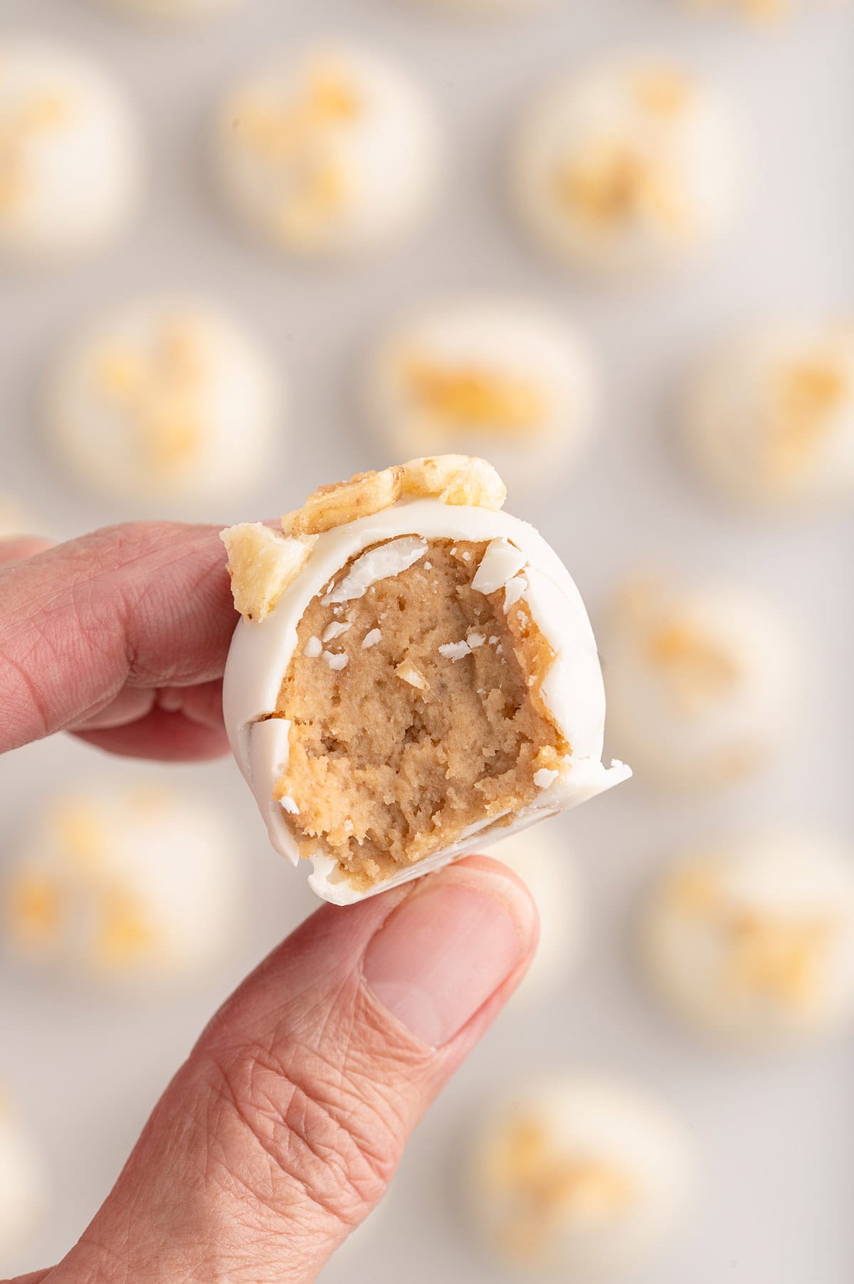 A hand holding a Banana Pudding Truffle with a bite taken out.