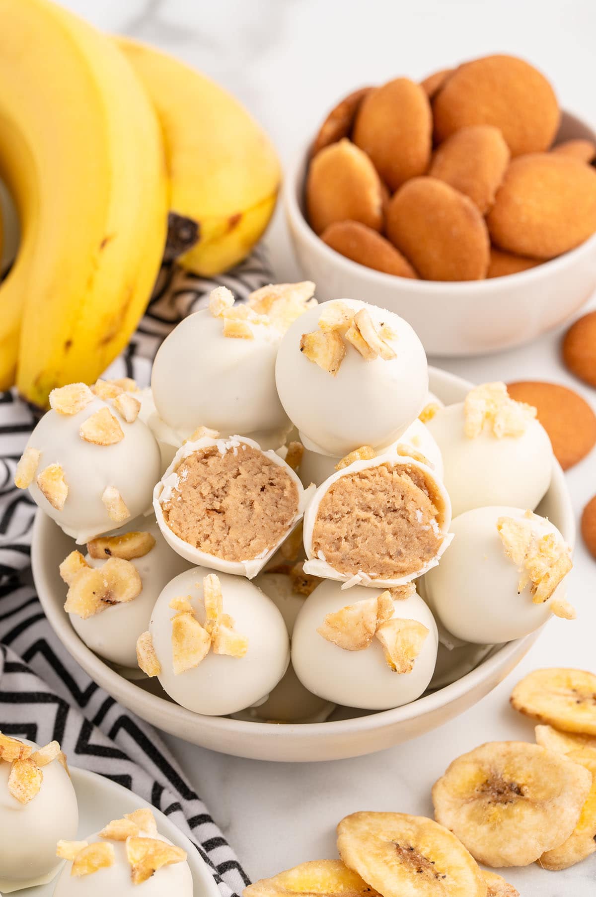 Bowl of Banana Pudding Truffles topped with banana chips with one truffle cut open to reveal the creamy filling.