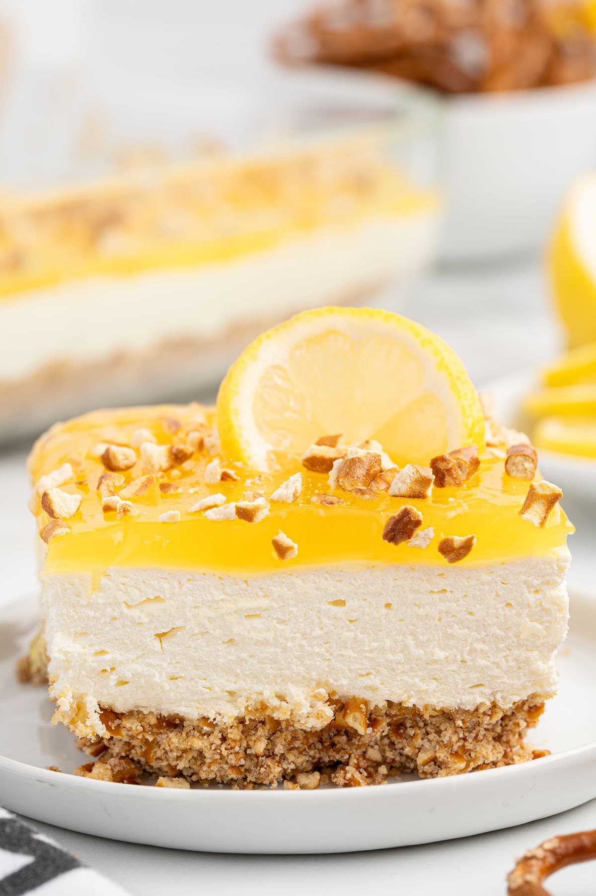 Lemon dessert slice with a pretzel crust, topped with lemon curd and a lemon slice garnish.