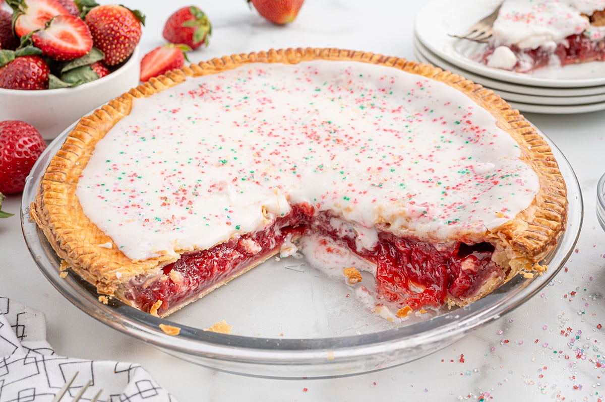 Strawberry Pop Tart Pie with icing and sprinkles, showing a slice removed.