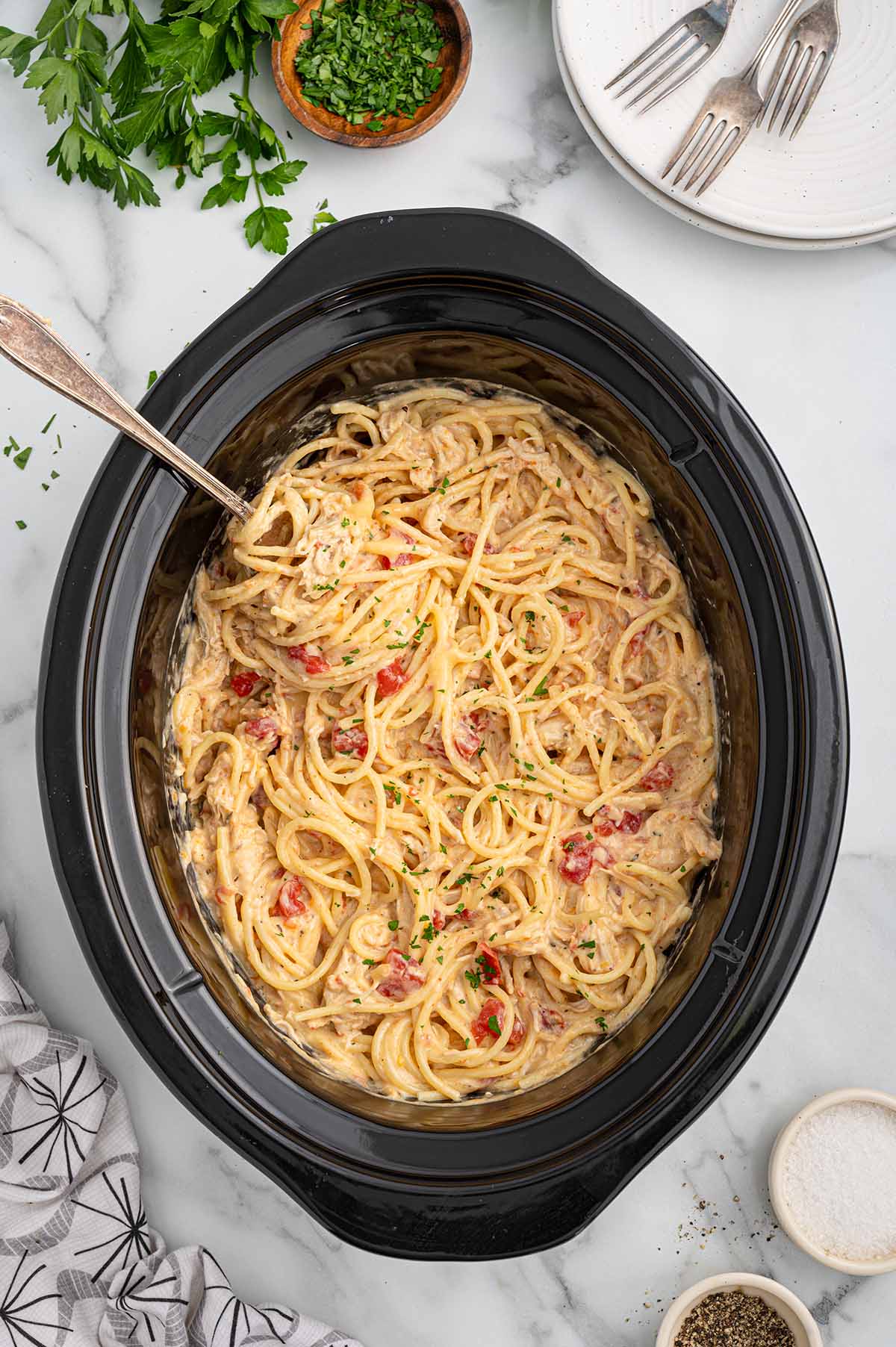 Slow cooker with creamy chicken spaghetti and garnished with parsley.