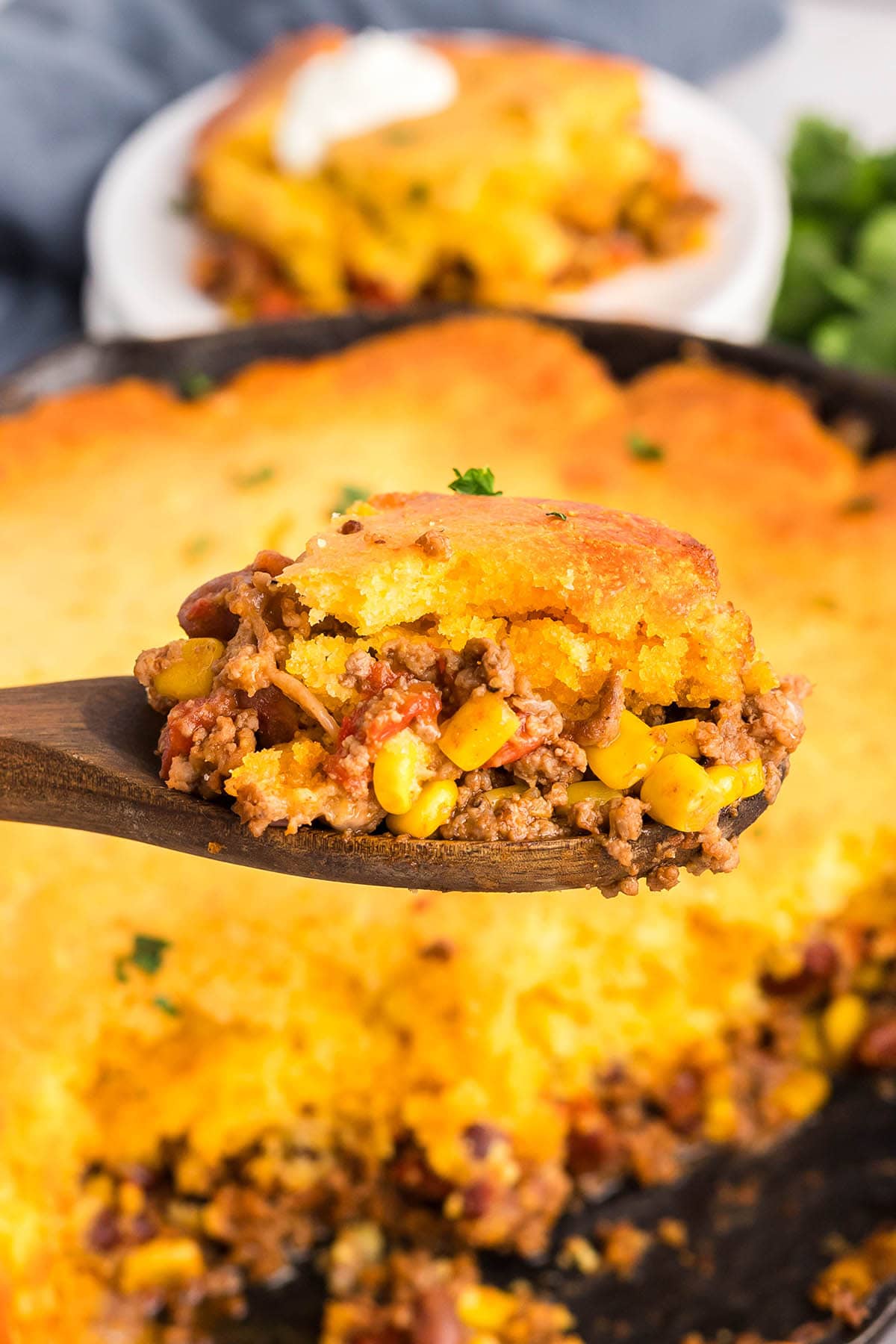 Wooden spoon scooping cornbread cowboy casserole with beef, corn, and beans.