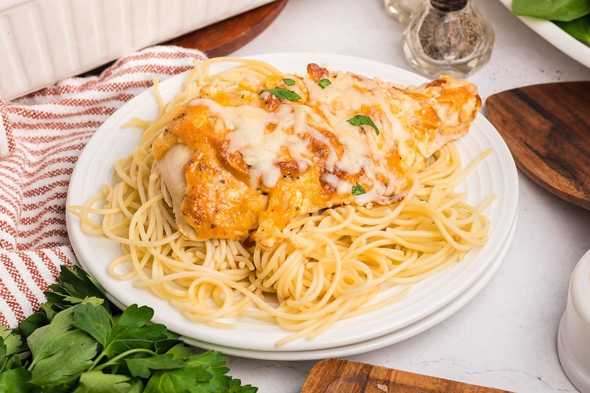 Melt in Your Mouth Chicken on a plate of spaghetti, garnished with fresh parsley.