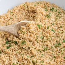 Bowl of seasoned rice garnished with chopped parsley and stirred with a wooden spoon.