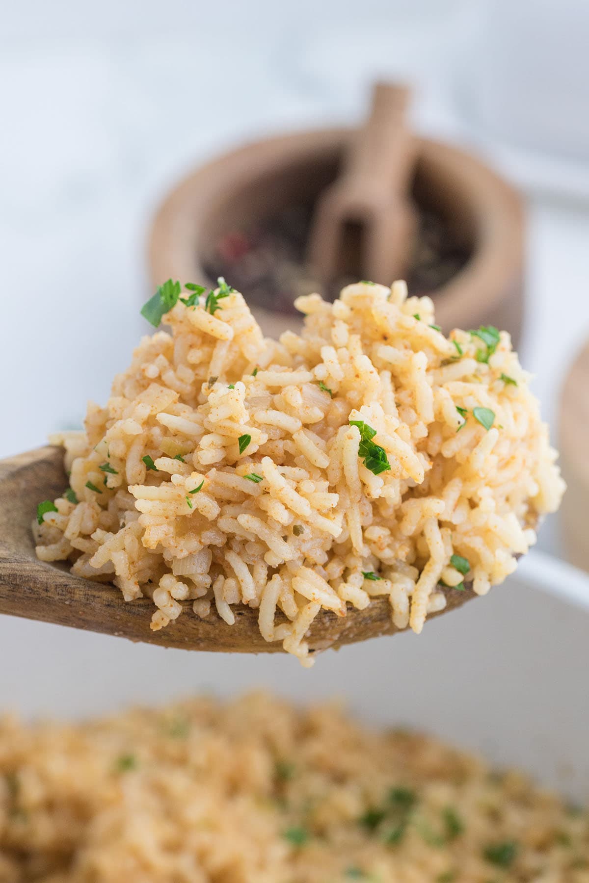 Wooden spoon holding seasoned rice with parsley.