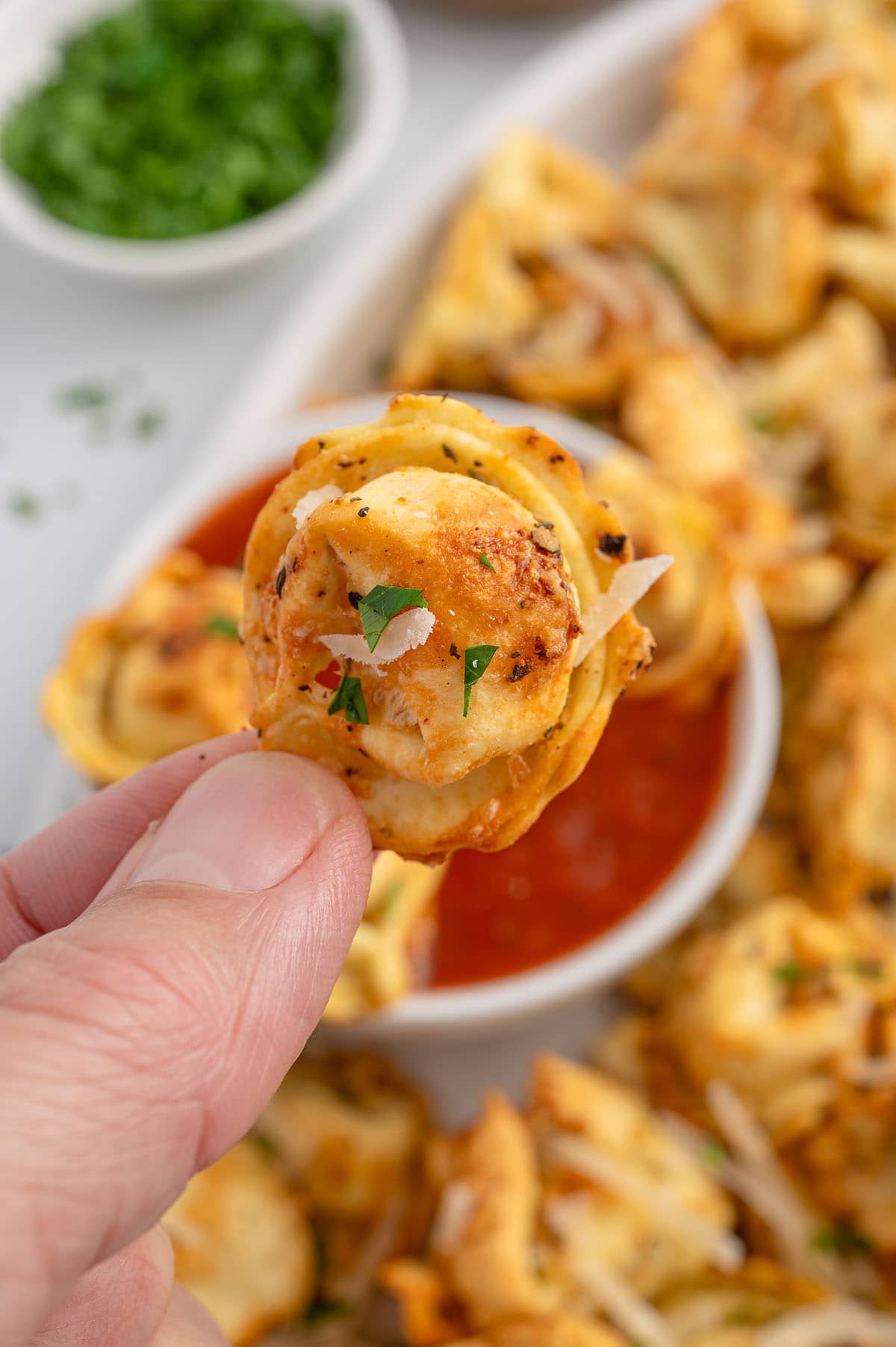 Hand holding a crispy air fryer tortellini with parmesan and parsley.