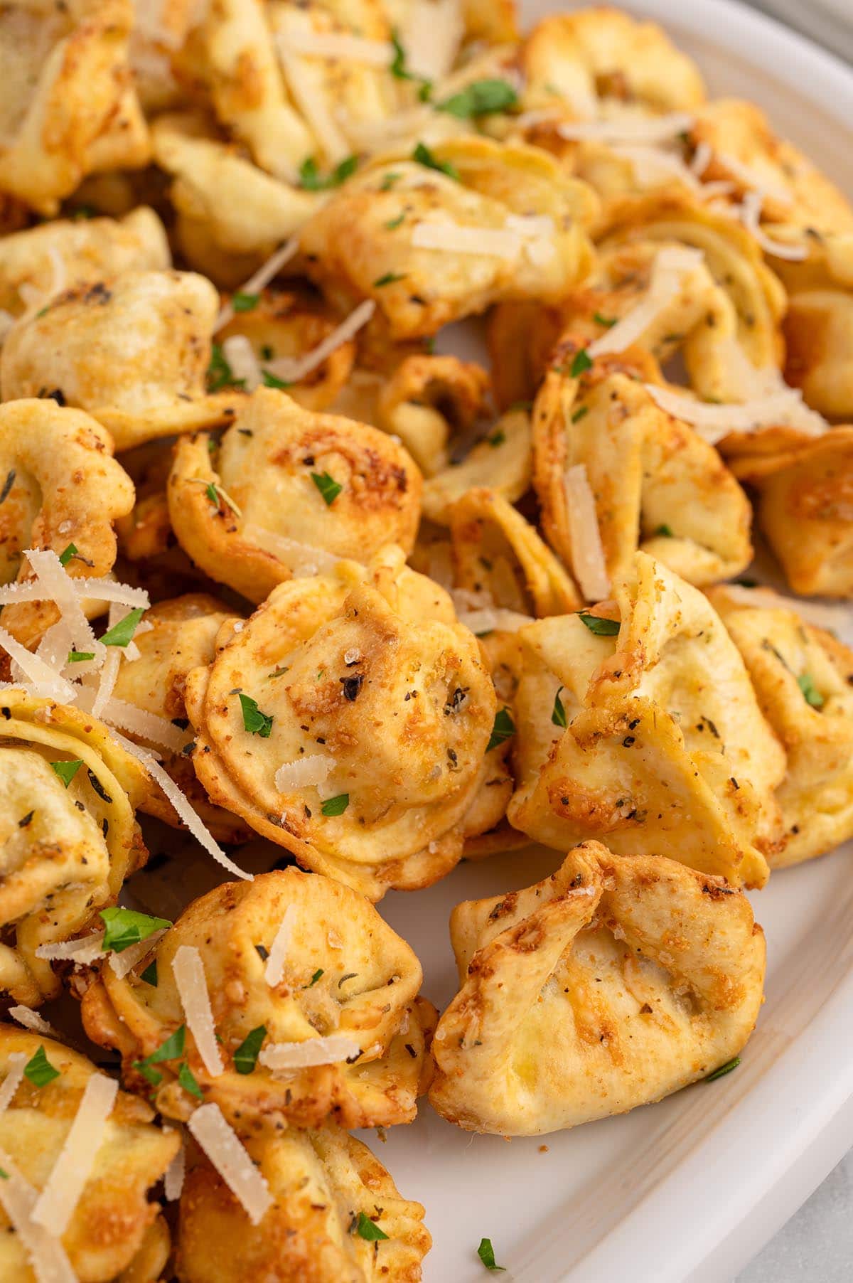 Crispy air fryer tortellini topped with parmesan and fresh parsley on a platter.