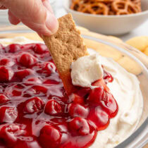 Cheesecake dip with cherry topping, scooped with a graham cracker.