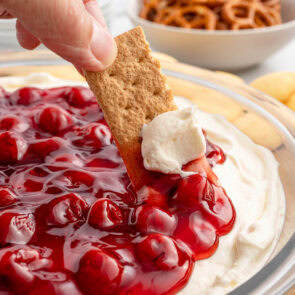 Cheesecake dip with cherry topping, scooped with a graham cracker.