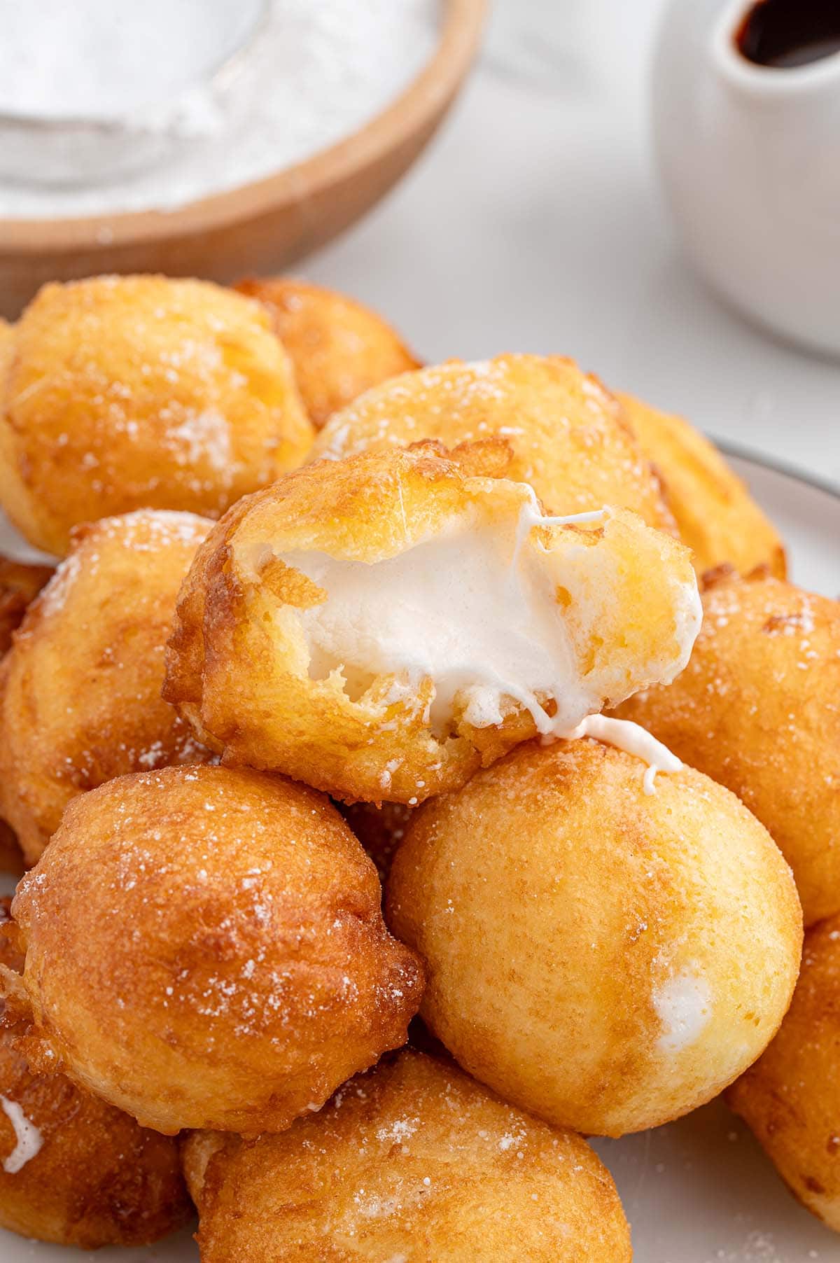 deep fried marshmallows stacked on a plate with one bite taken out showing the melted marshmallow inside. 