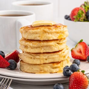 Stack of fluffy pancakes topped with butter and syrup.