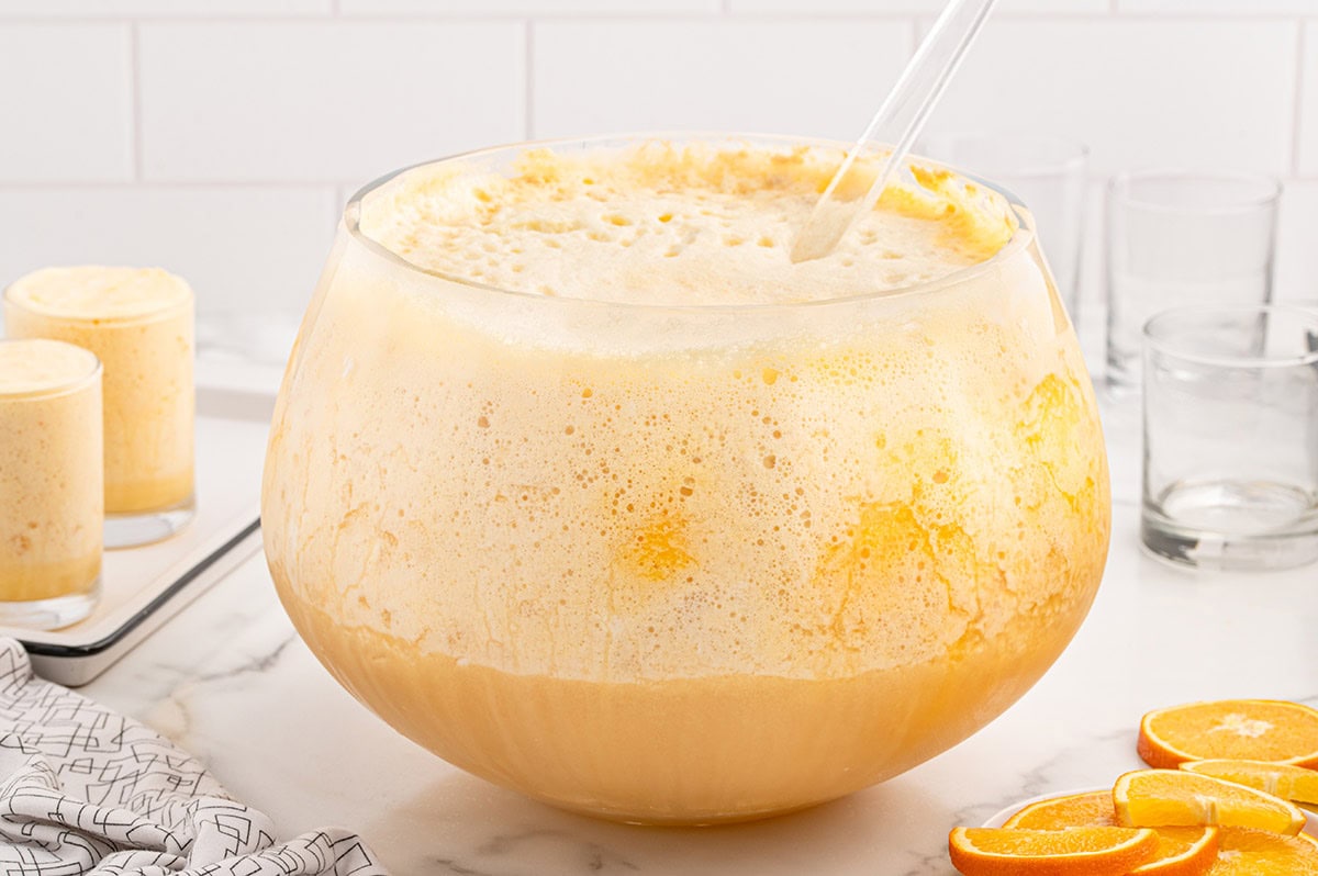 Orange Dreamsicle Punch in a large glass bowl with a ladle.