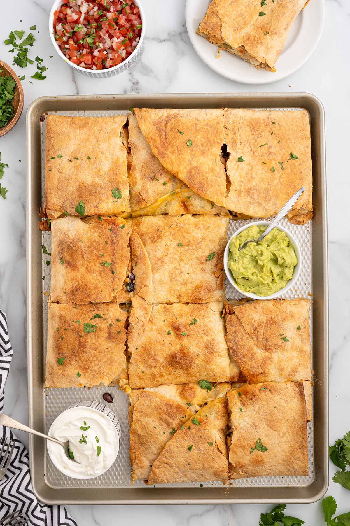 Sheet pan chicken quesadillas cut into squares, served with guacamole, sour cream, and pico de gallo.