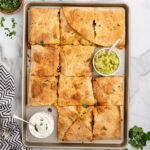 Sheet pan chicken quesadillas cut into squares, served with guacamole and sour cream.