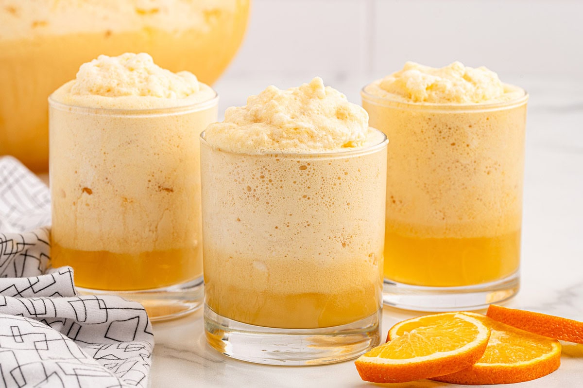 Three glasses of Orange Dreamsicle Punch with frothy tops, garnished with orange slices.