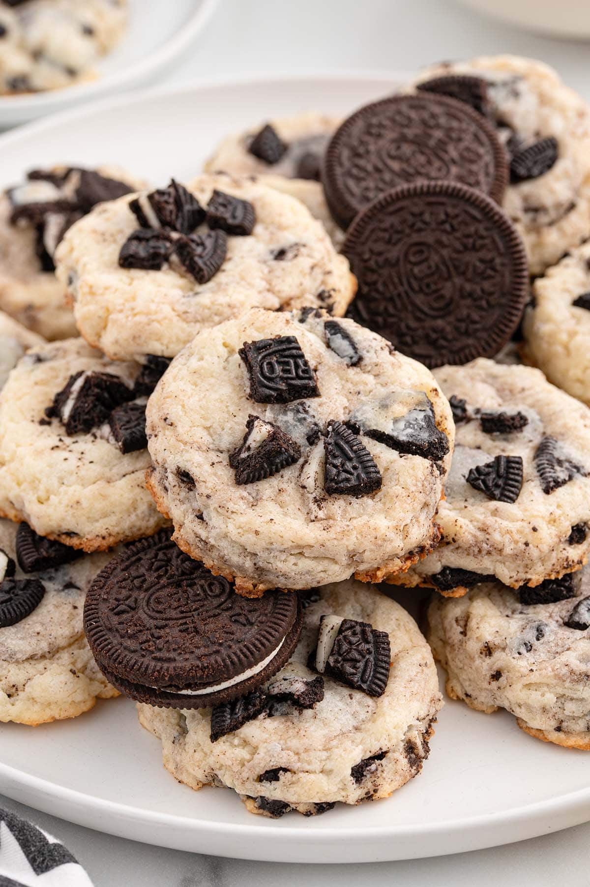 A plate of Oreo Cheesecake Cookies topped with crushed Oreos, surrounded by whole Oreo cookies.