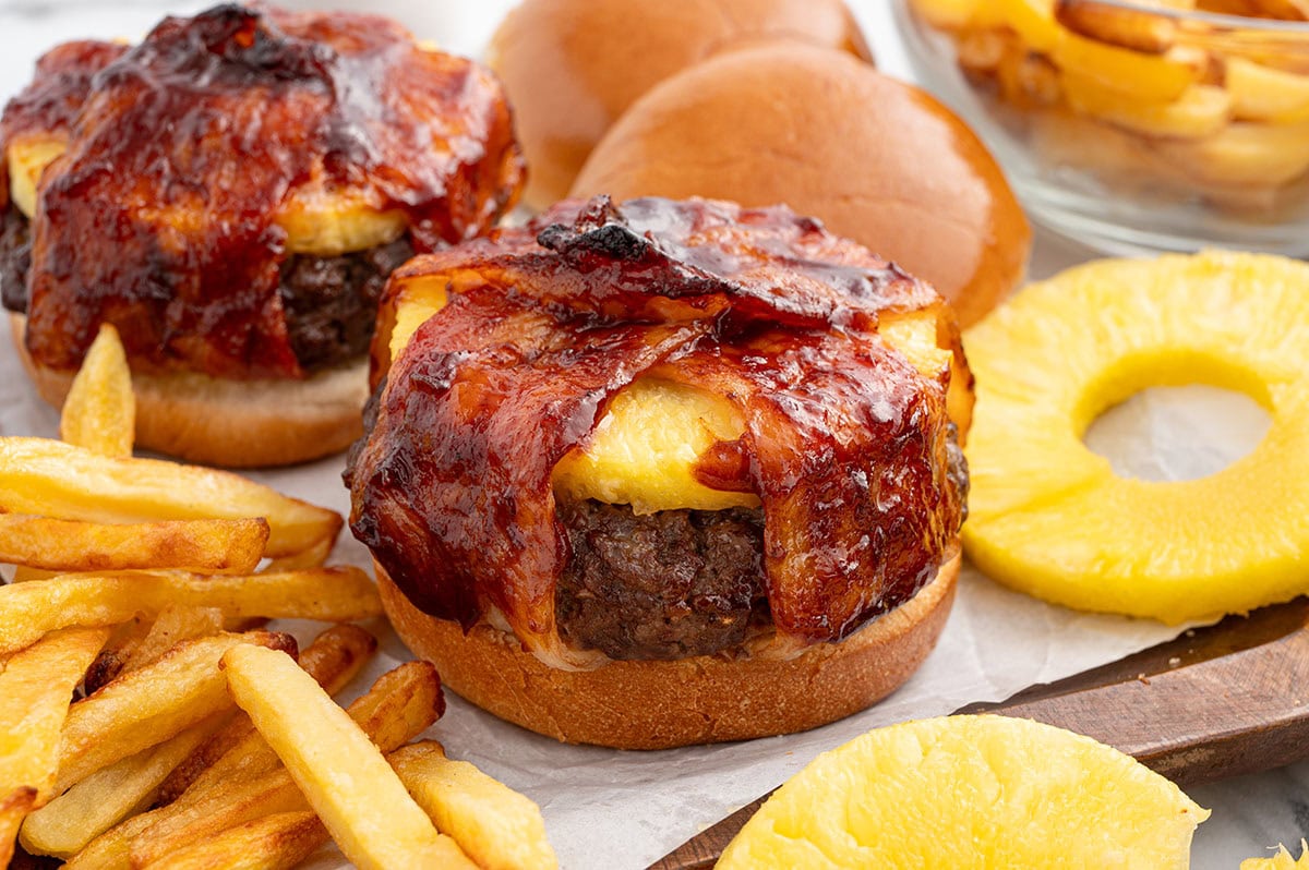 pineapple bacon burger on top of wooden board with fries. 