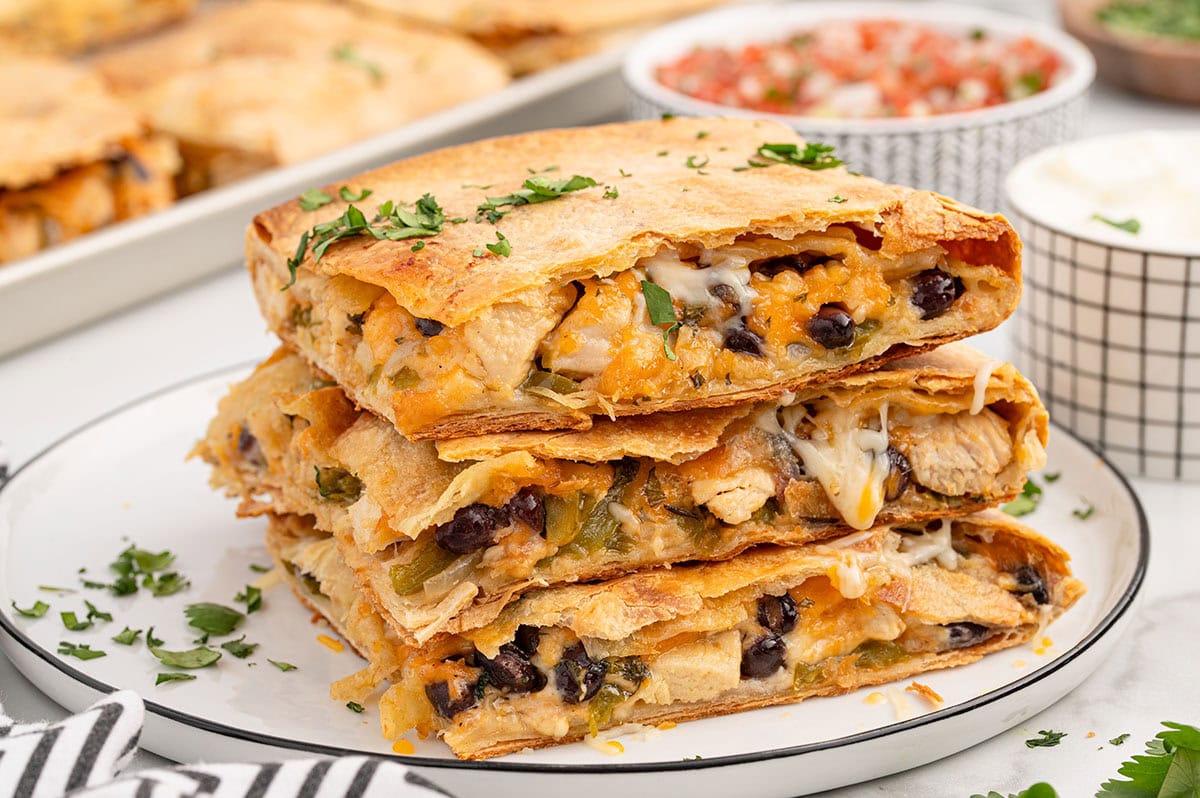 Stack of sheet pan chicken quesadilla slices with melted cheese, black beans, and crispy tortillas.