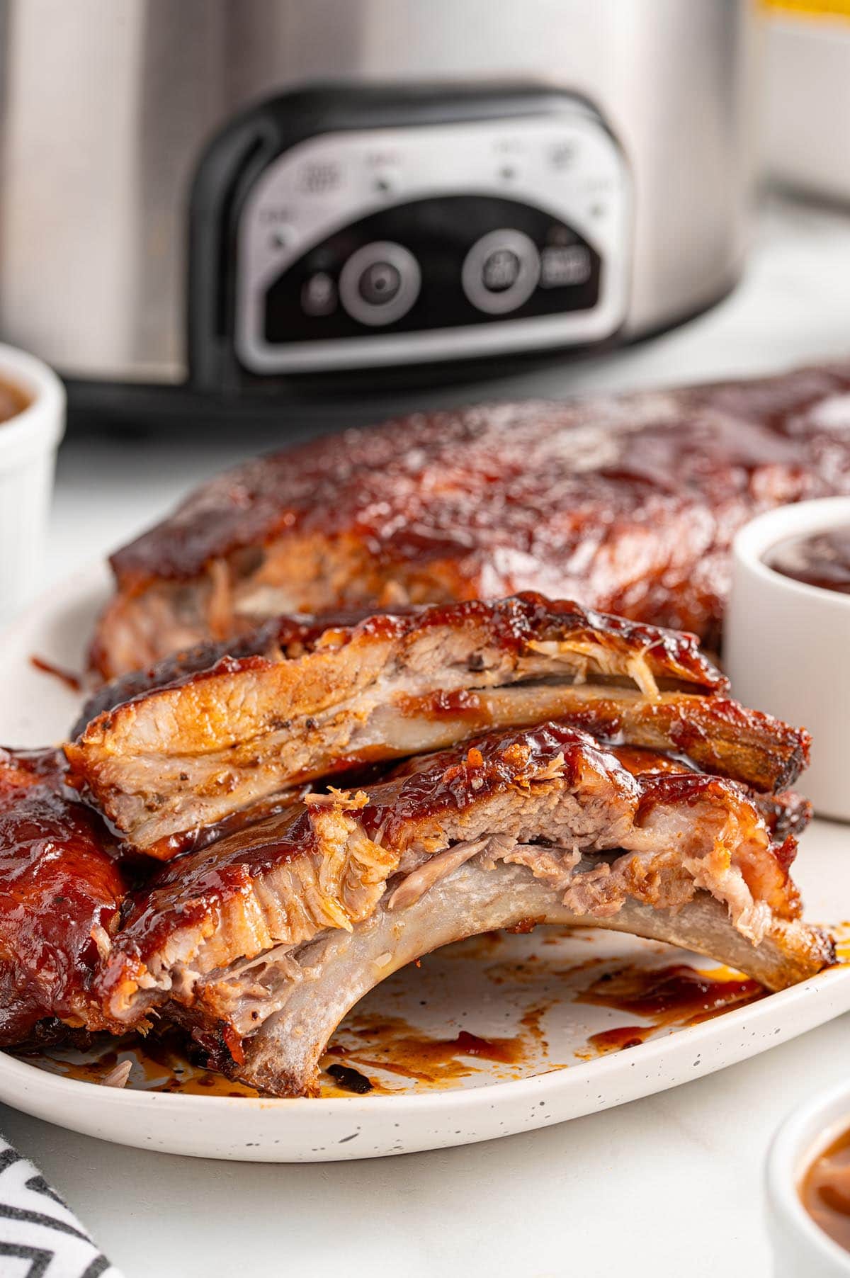 Slow Cooker Baby Back Ribs with barbecue sauce on a plate, slow cooker in the background.