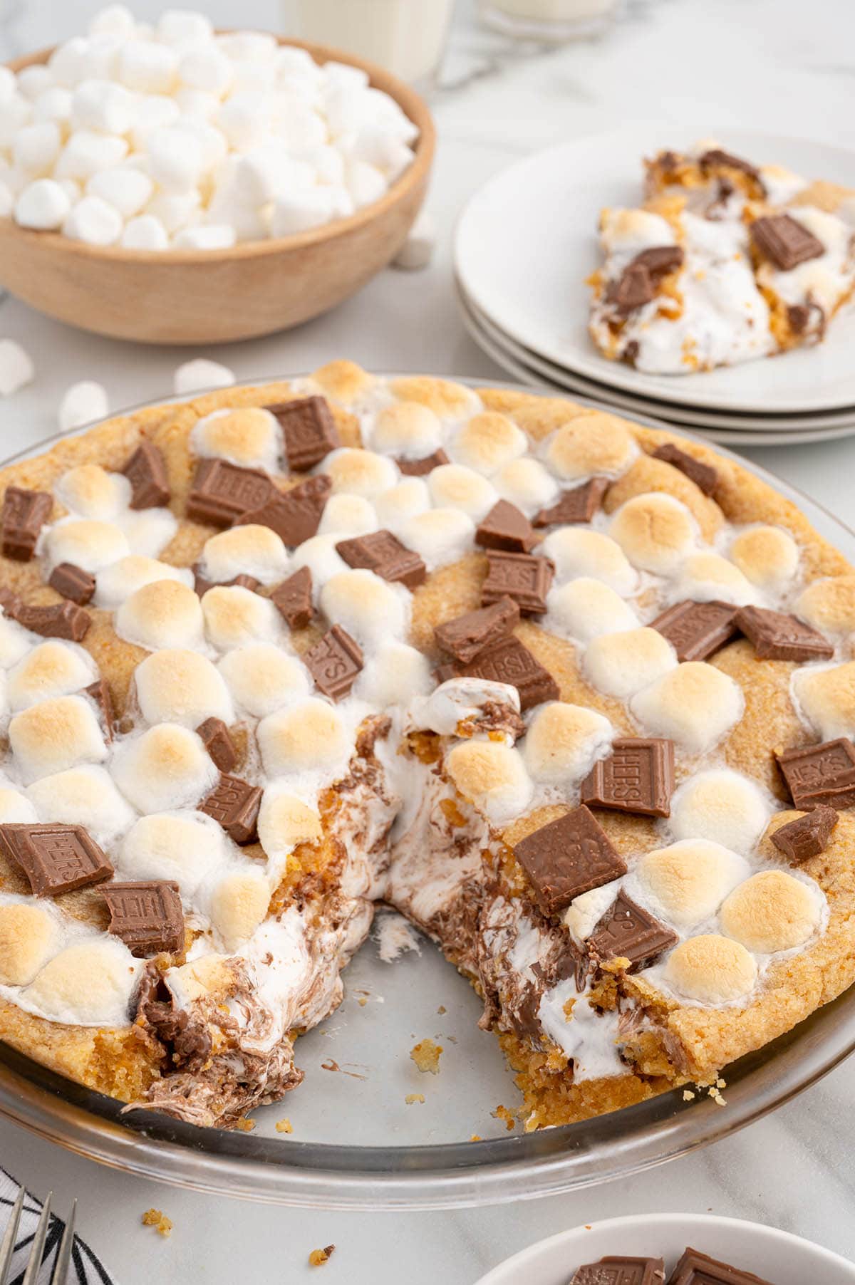 Sliced s'mores pie with toasted marshmallows and melted chocolate in a glass pie dish.