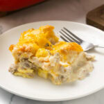 Biscuits and gravy casserole with sausage, eggs, and melted cheese on a white plate.