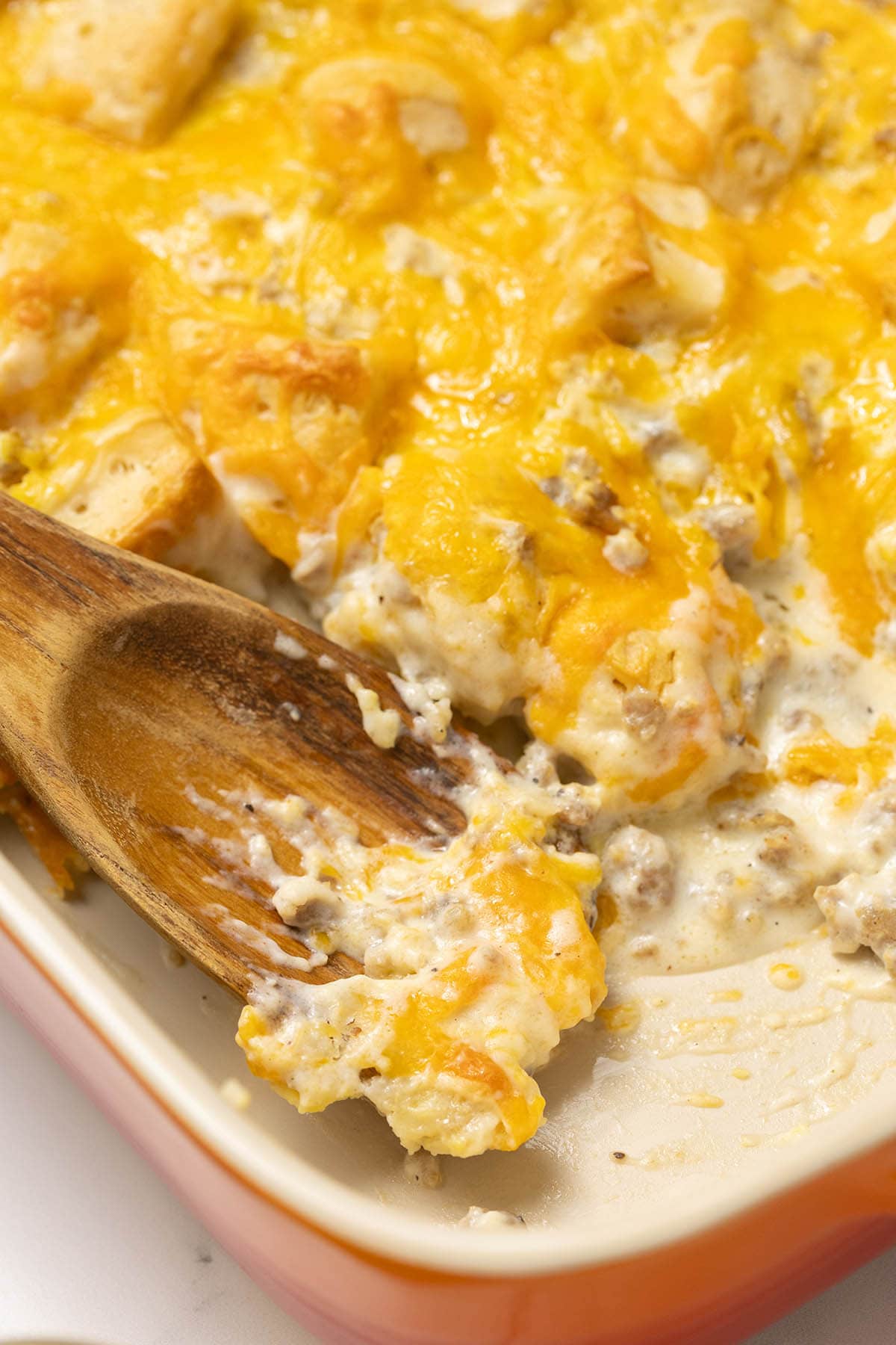 Biscuits and gravy casserole in a baking dish with a wooden spoon scooping a serving.