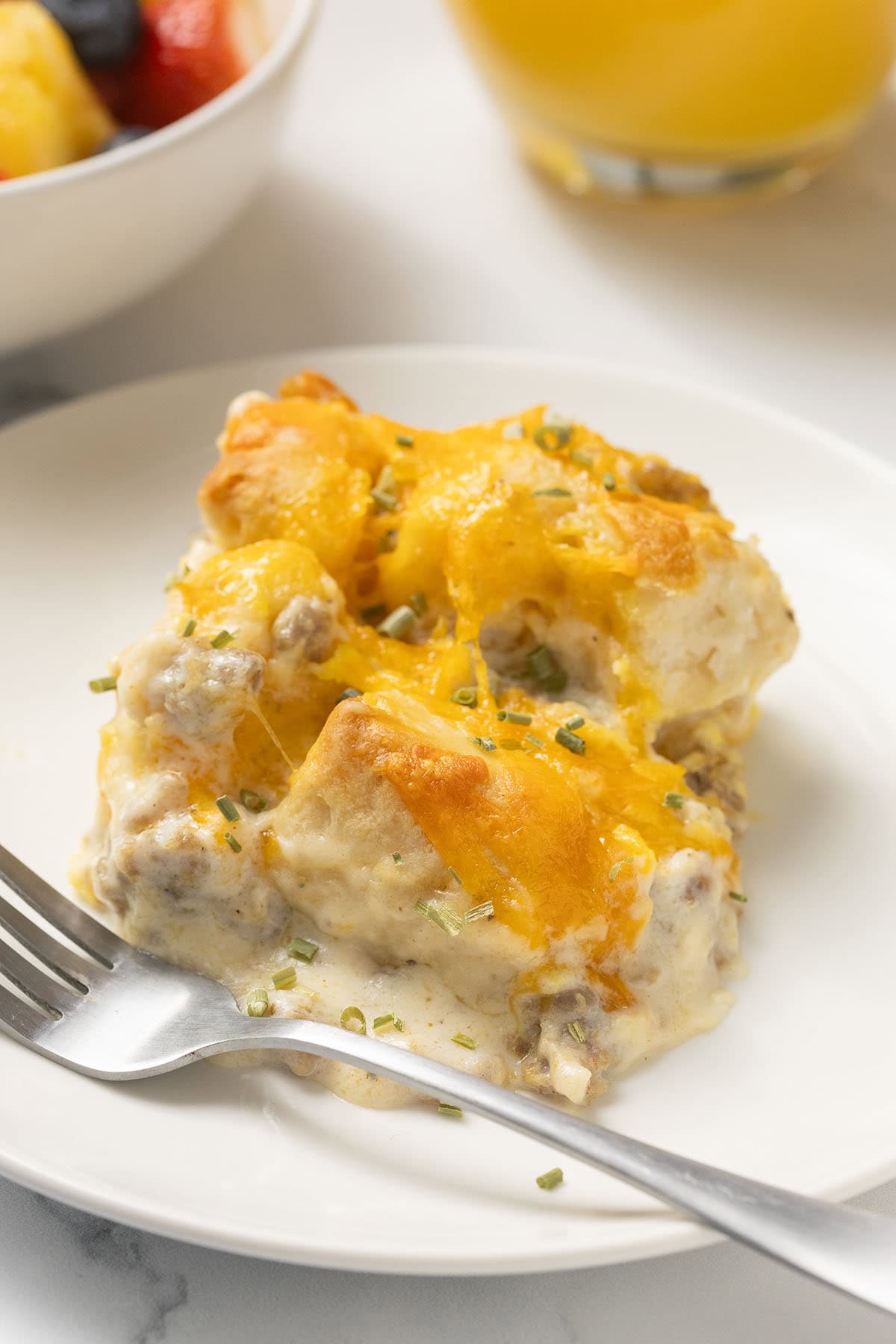 Biscuits and gravy casserole served on a white plate, topped with melted cheese and chopped chives.