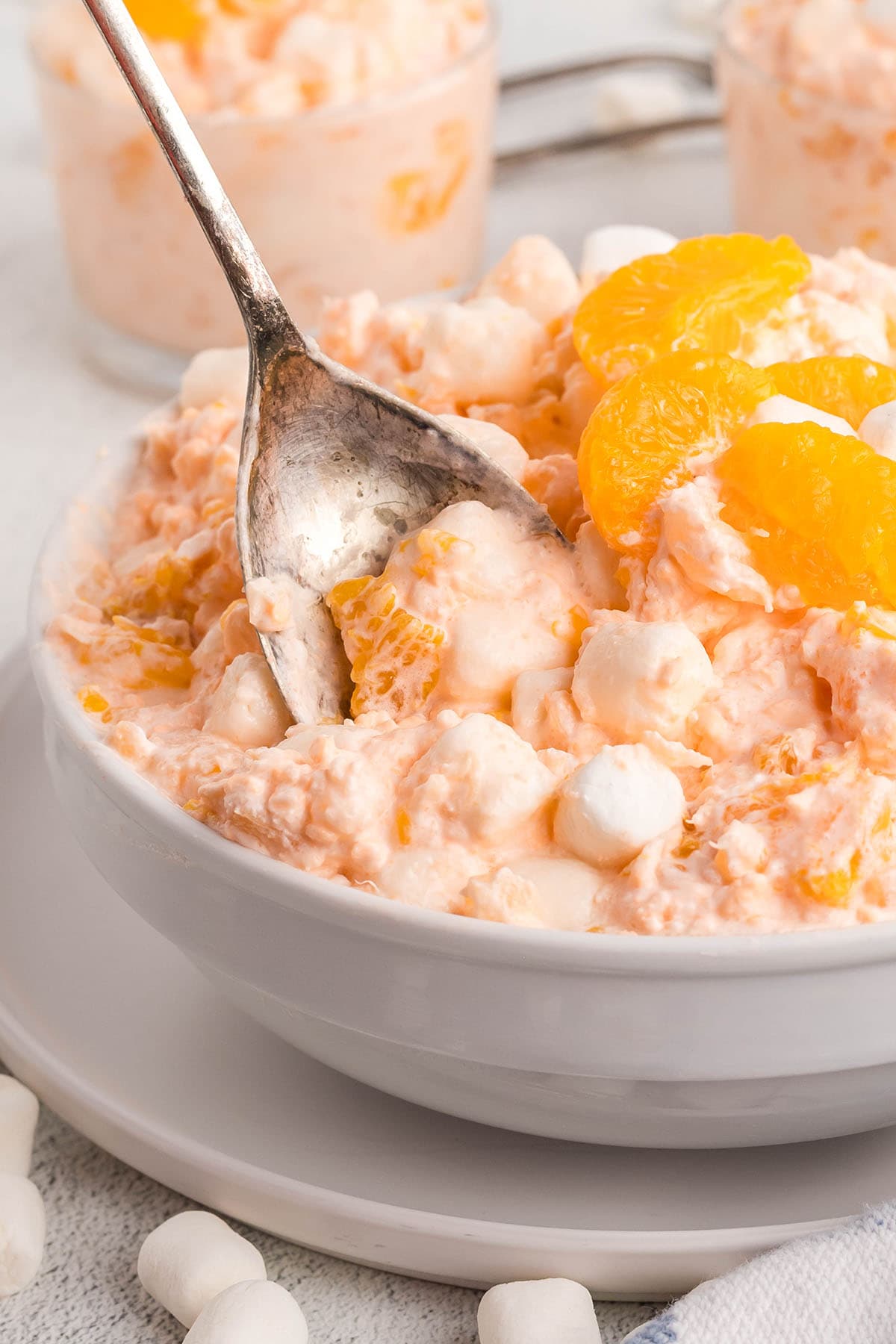 Bowl of cottage cheese Jello salad with mandarin oranges and mini marshmallows, spoon scooping.