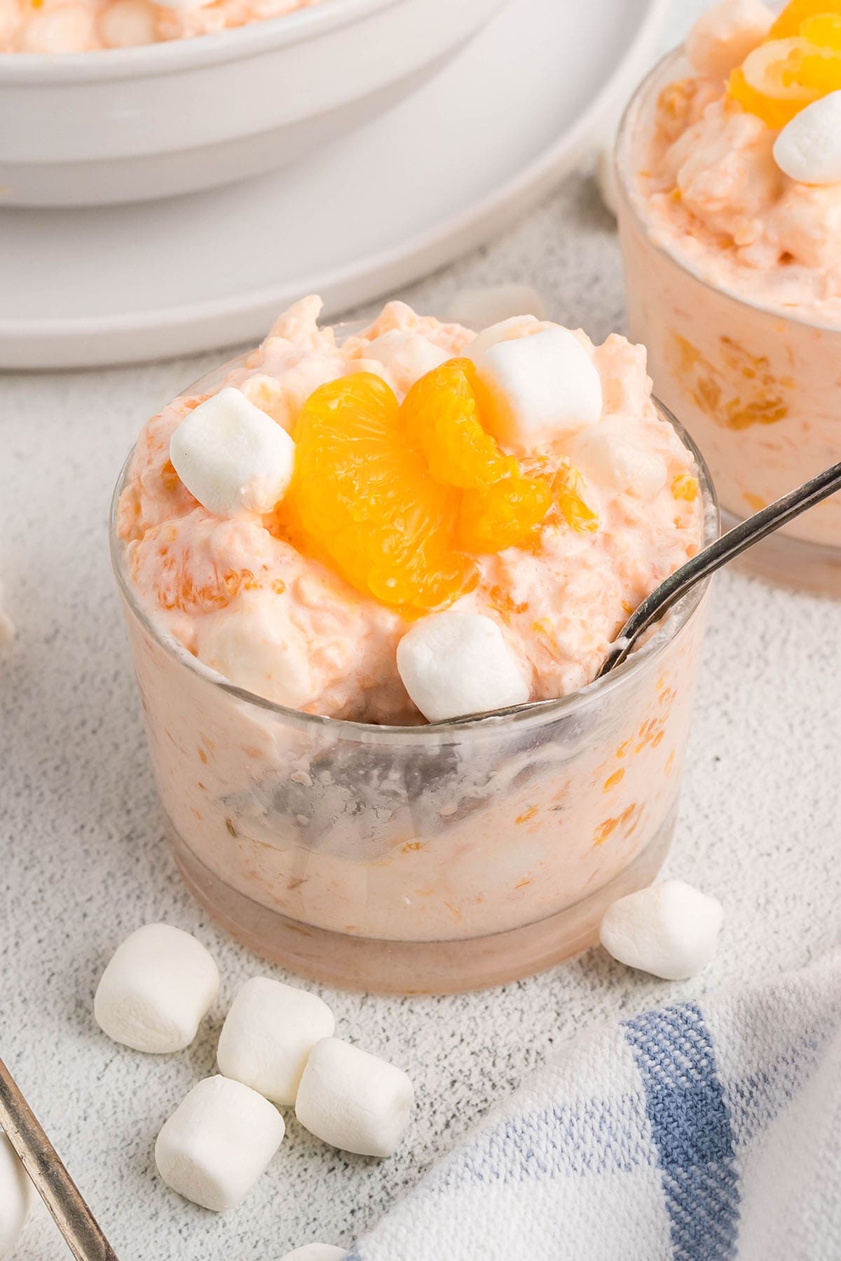 Small glass of cottage cheese Jello salad topped with mandarin oranges and mini marshmallows.
