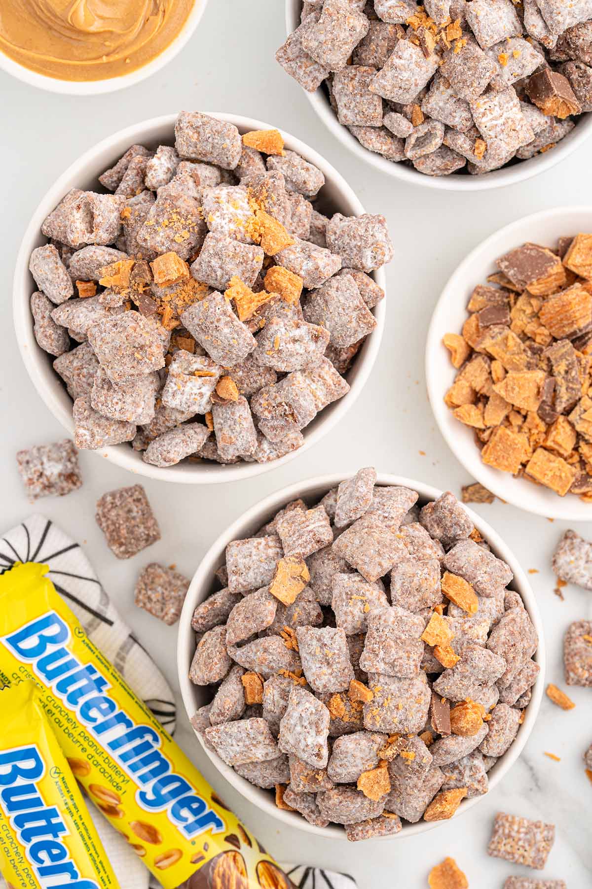 Bowls of Butterfinger Puppy Chow with crushed Butterfinger pieces and candy bars.