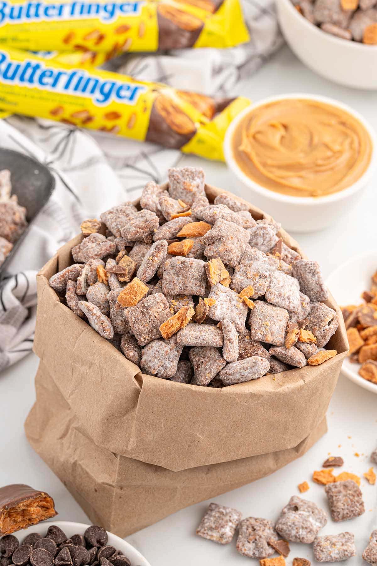 Butterfinger Puppy Chow in a brown paper bag with candy bars and peanut butter nearby.