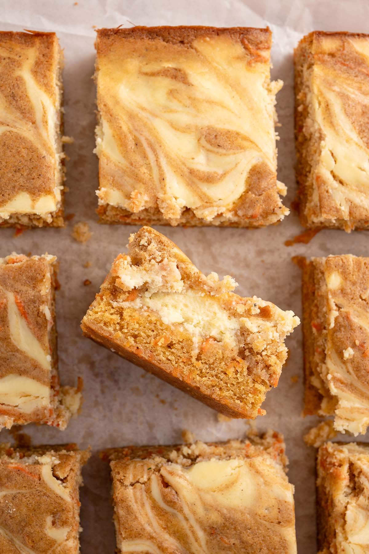 Overhead view of carrot cake bars with a cheesecake swirl, one piece tilted to reveal its texture.