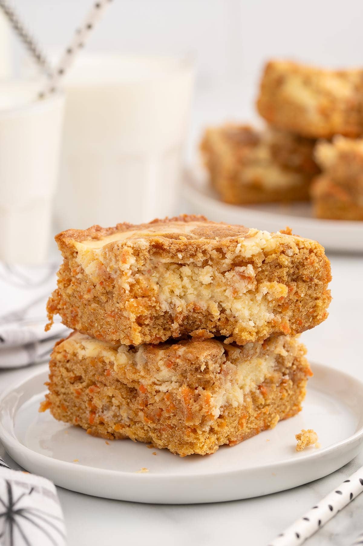 Stacked carrot cake bars with a creamy cheesecake swirl on a white plate.