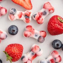 Frozen yogurt dog treats with strawberries and blueberries, shaped like bones.