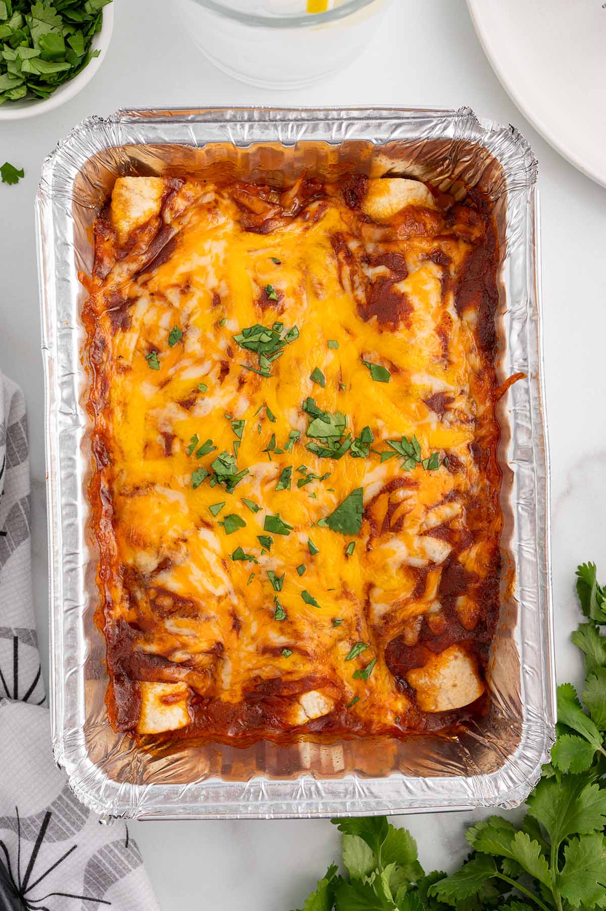 Freezer Enchiladas in a foil pan with melted cheese and cilantro.