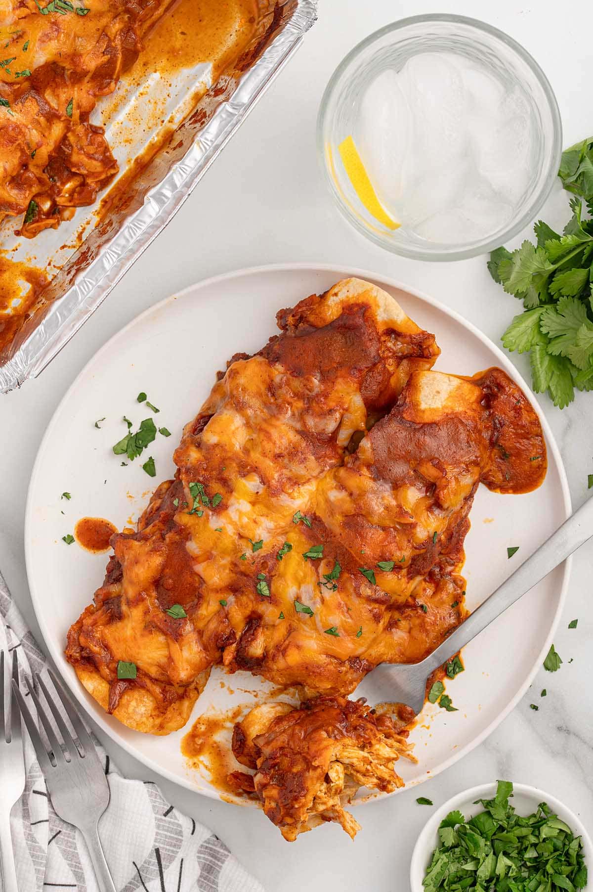 Freezer Enchiladas served on a white plate with melted cheese and enchilada sauce, garnished with cilantro.