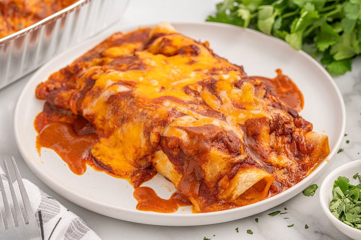 Freezer Enchiladas topped with melted cheese and enchilada sauce on a white plate.