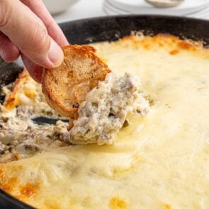 Philly cheesesteak dip scooped with a toasted baguette slice from a skillet with melted cheese.