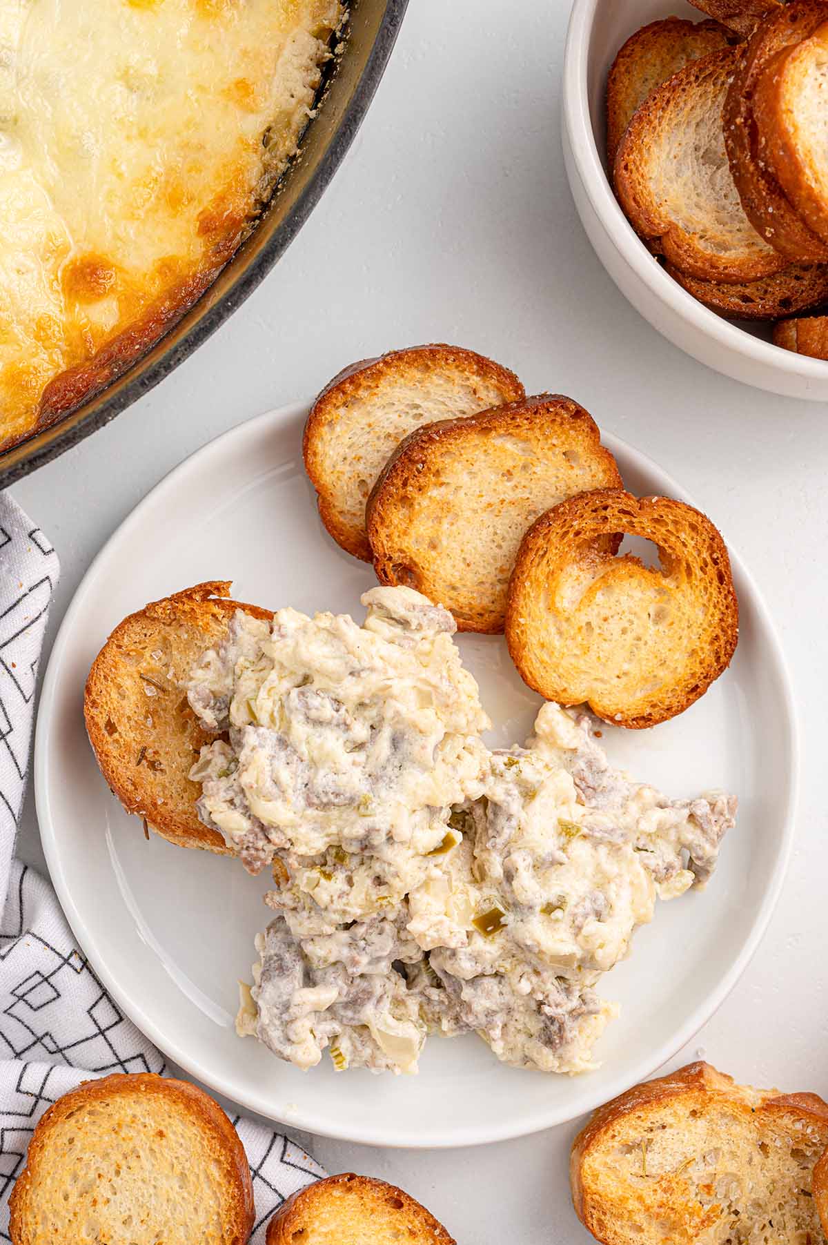 Philly cheesesteak dip on a plate with toasted baguette slices.