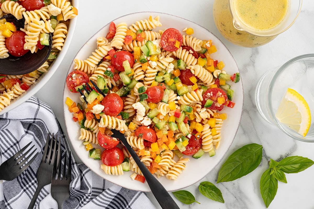 Rotini pasta salad with tomatoes, cucumbers, peppers, and feta on a plate.