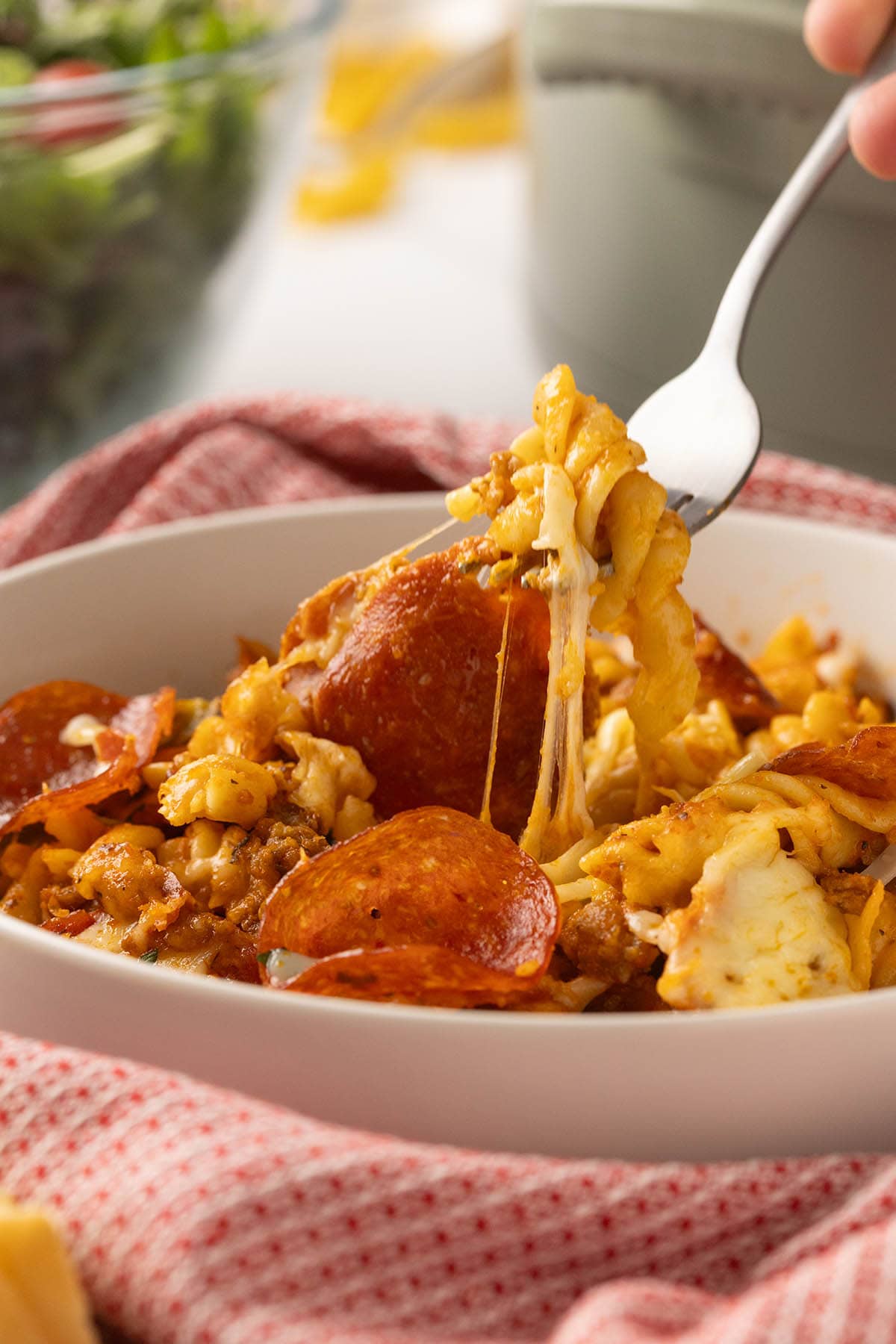 Close-up of cheesy crock pot pizza pasta with pepperoni being lifted by a fork.