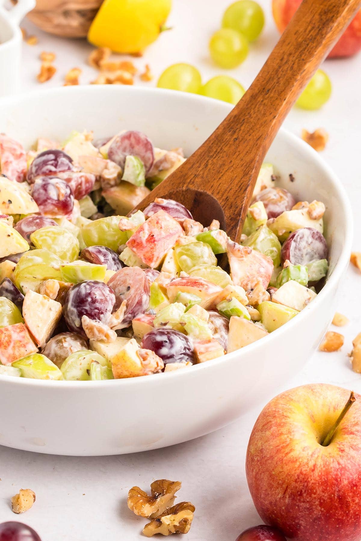 Waldorf salad with grapes, apples, celery, and walnuts in a white bowl with a wooden spoon.