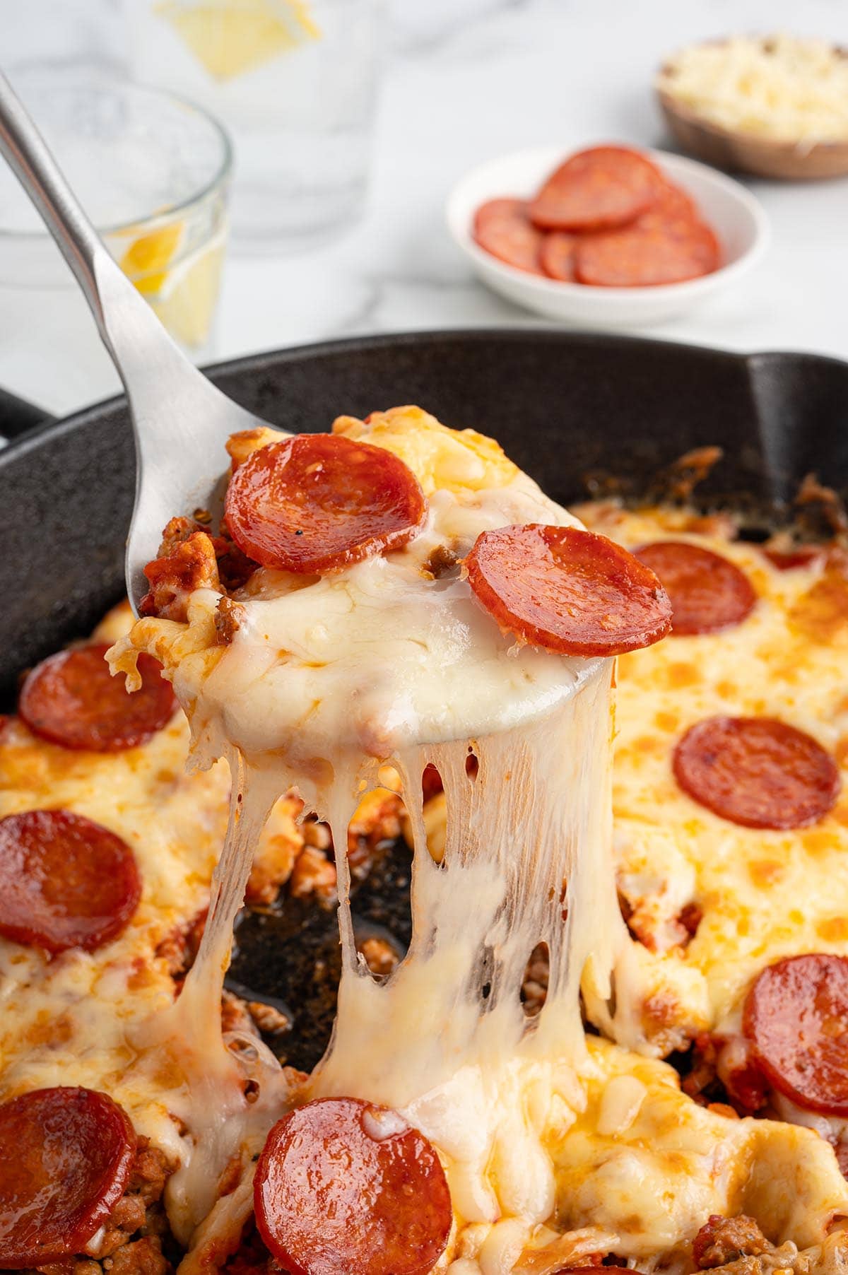 Cheesy slice of crustless pepperoni pizza being lifted from a skillet with gooey melted cheese.