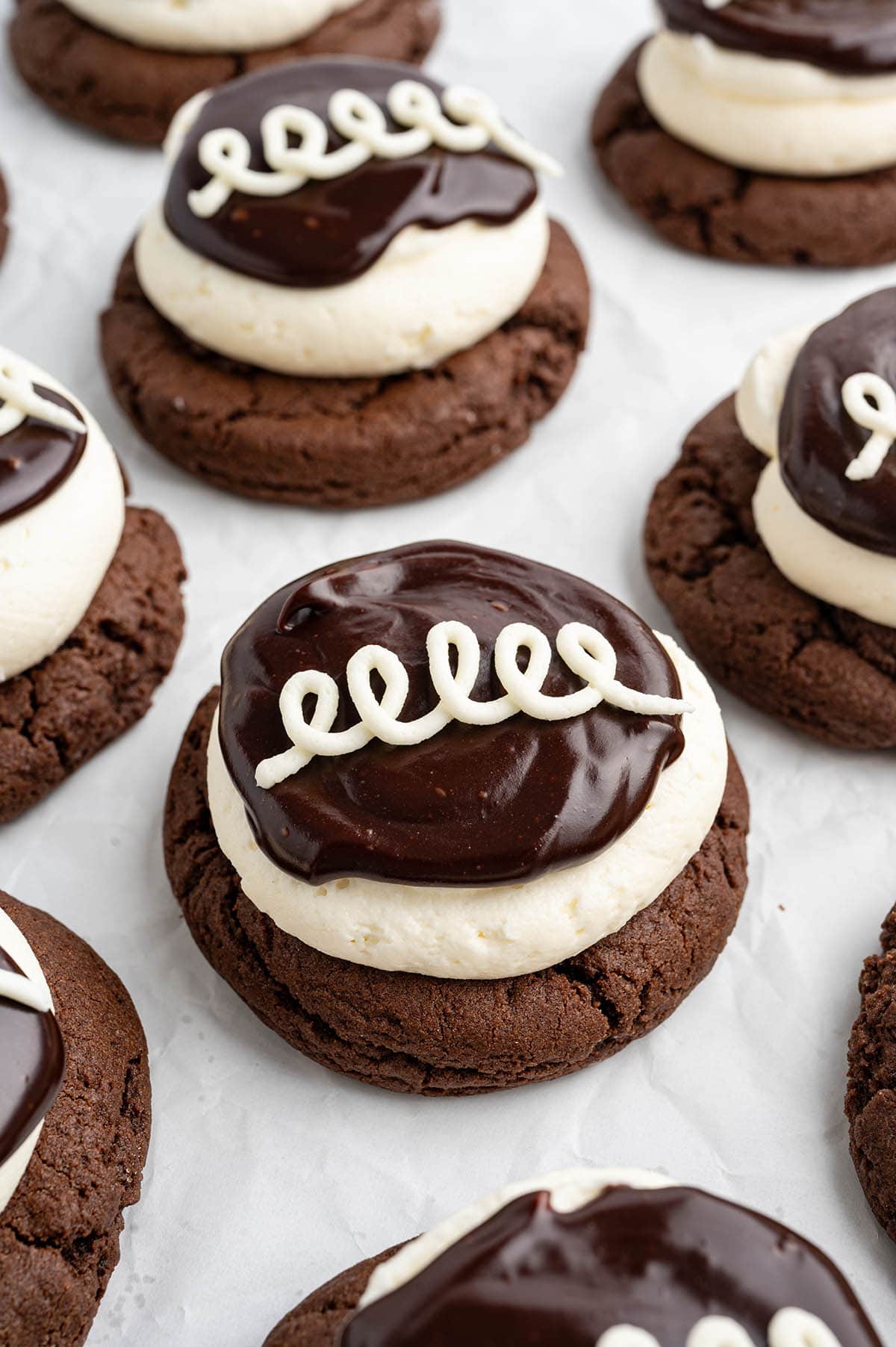 A tray of chocolate cookies topped with fluffy cream, chocolate ganache, and a classic white icing swirl, inspired by Hostess cupcakes.