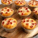 Mini pizza pot pies baked in foil cups, topped with melted cheese and mini pepperoni slices, arranged on a wooden serving board.