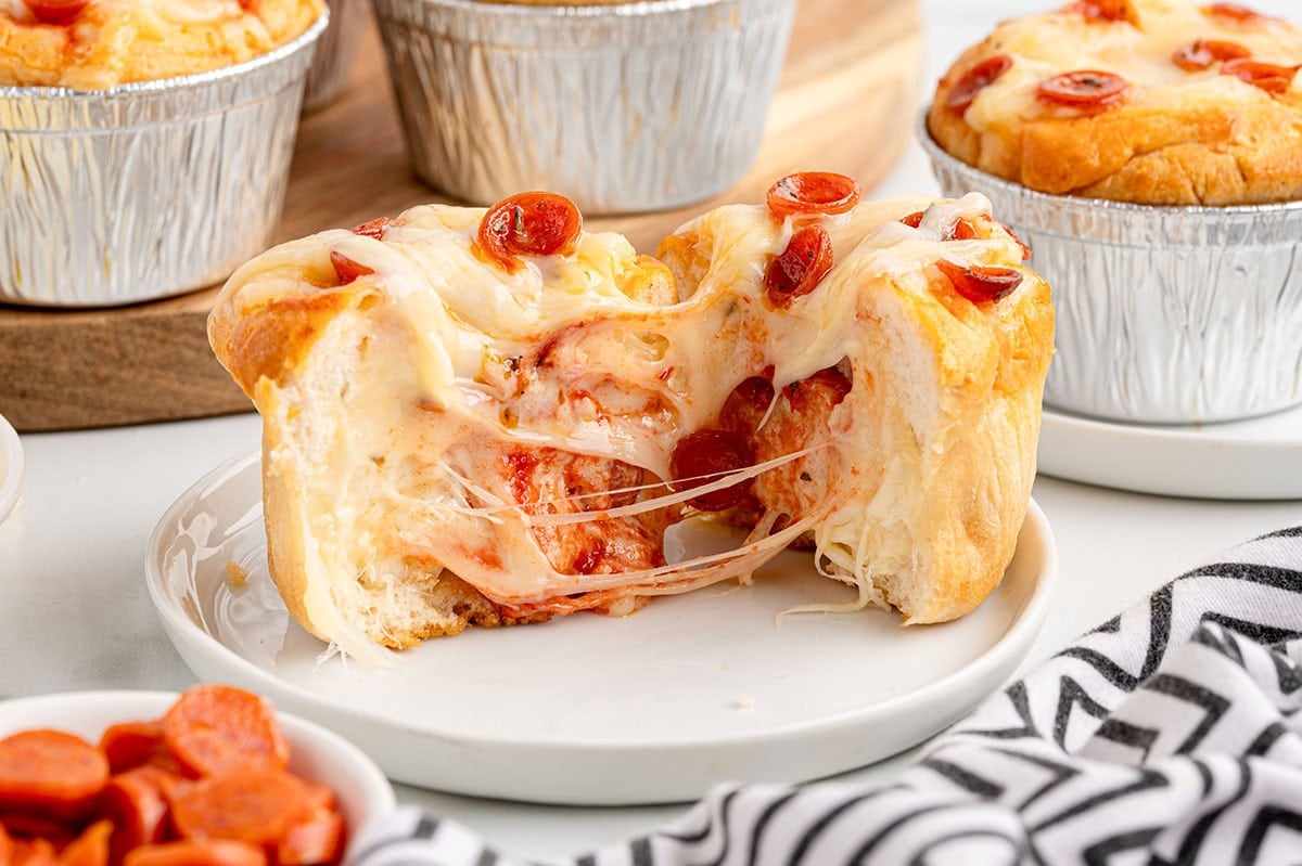 Mini pizza pot pie cut in half, showing gooey melted cheese, pizza sauce, and mini pepperonis inside a fluffy biscuit crust.